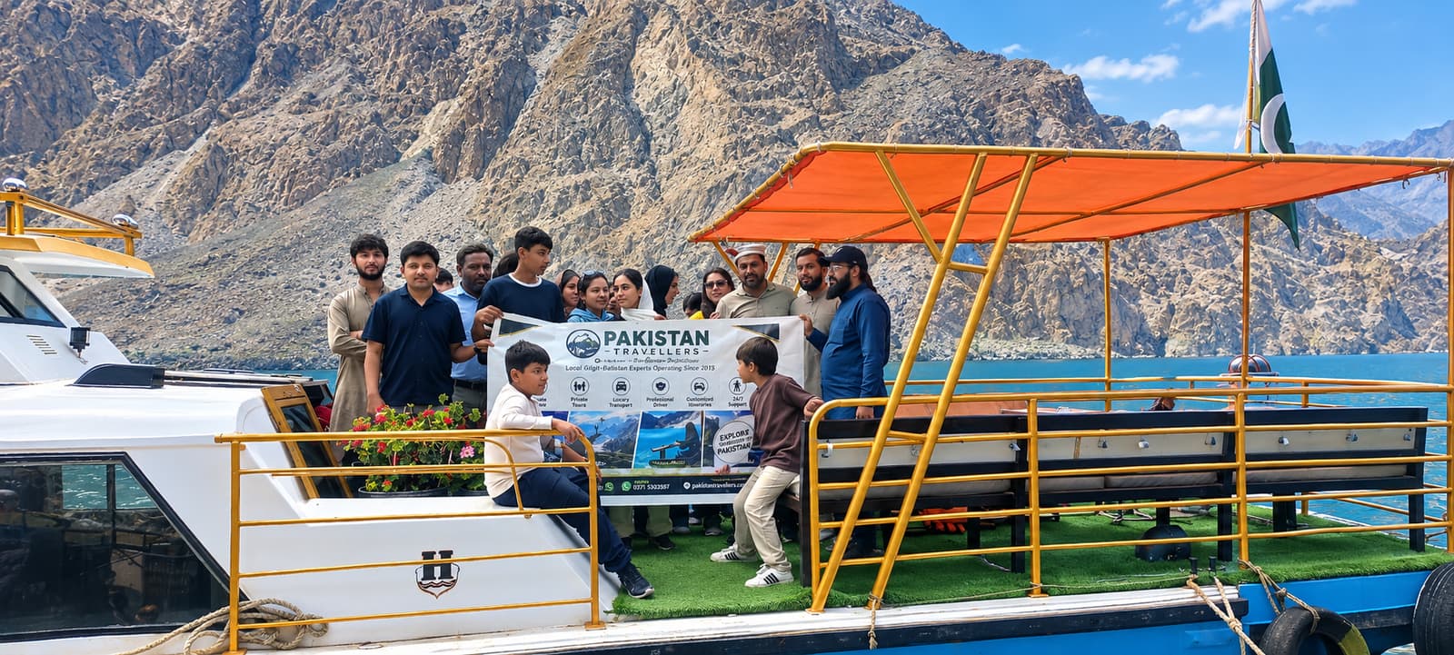 A family group on a boat on Attabad Lake in Hunza holding a Pakistan Travellers banner